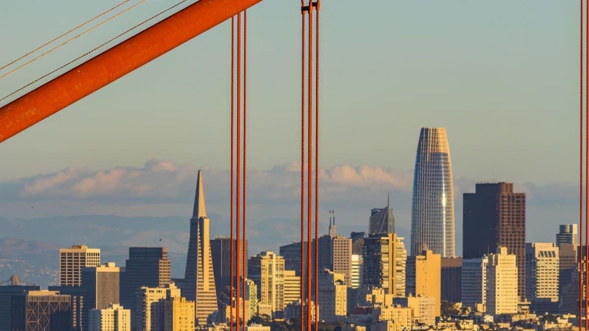 Golden Gate Bridge cables framing San Francisco skyline at sunset.