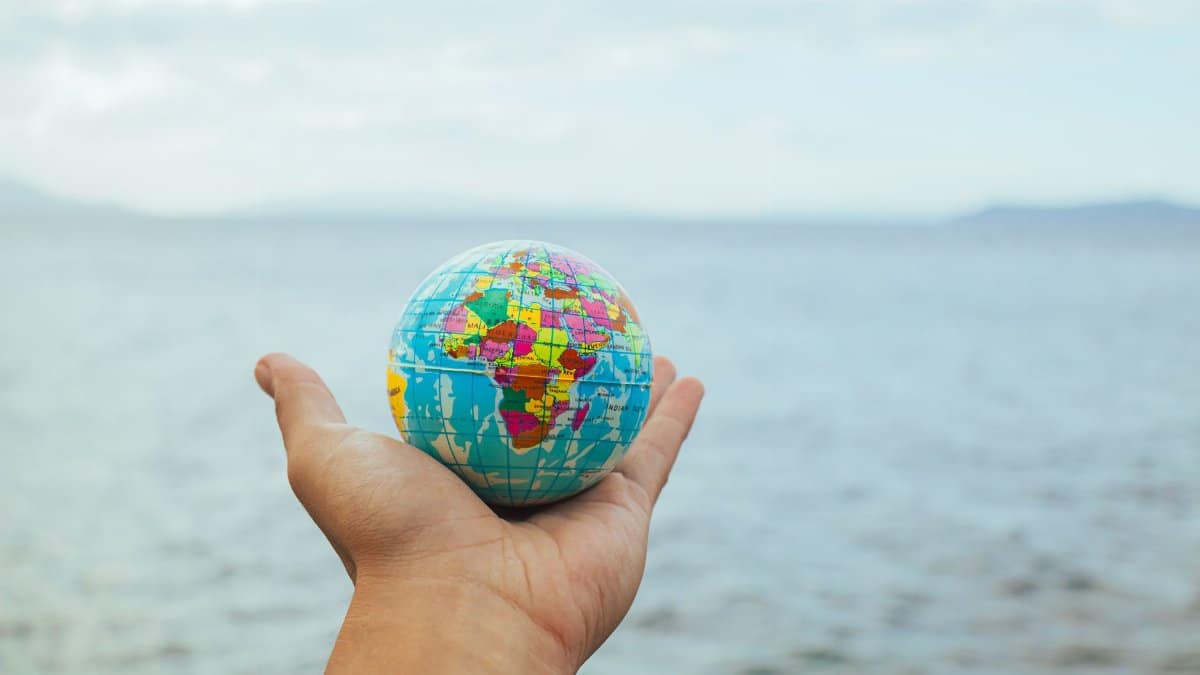 A hand holding a small globe with an ocean backdrop, symbolizing global connection and travel.