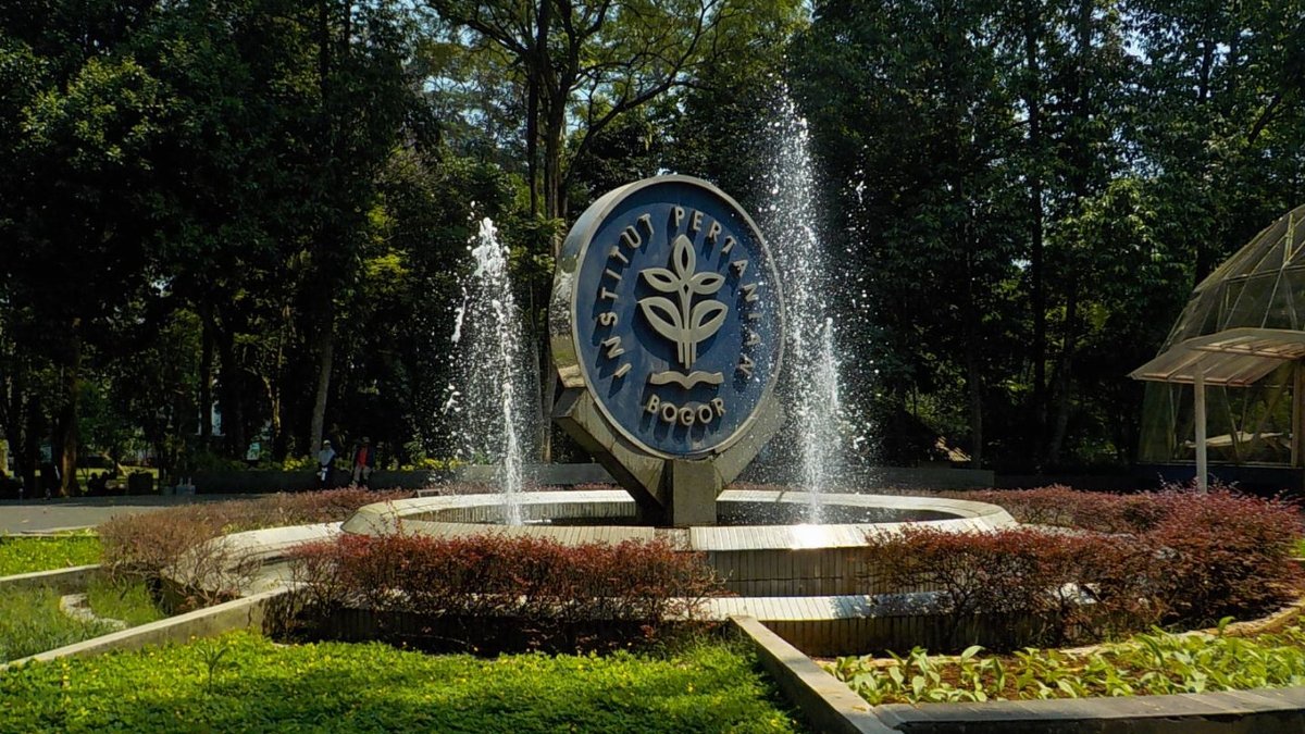 Fountain with the Institut Pertanian Bogor emblem surrounded by vibrant greenery and trees.