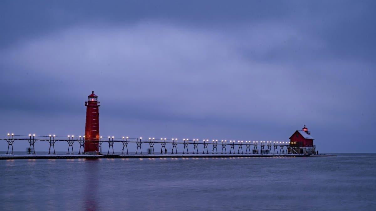 A serene winter evening view of a lighthouse on Lake Michigan with a calm blue sky.