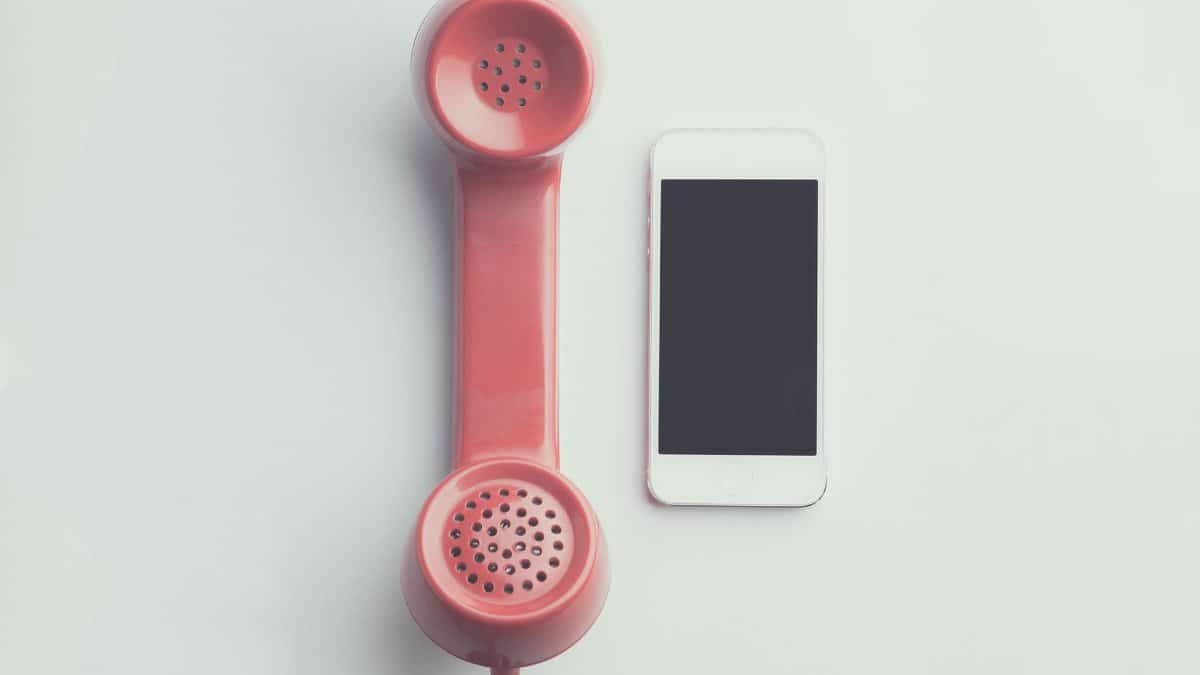 Comparison of a vintage pink telephone receiver and a modern smartphone on a simple backdrop.