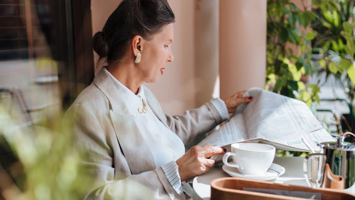 Sophisticated woman reading newspaper at a cafe table with coffee.