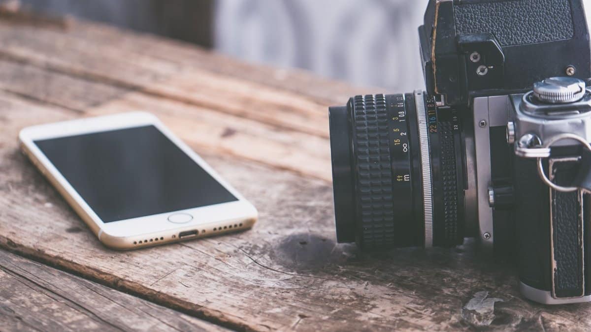 A vintage camera alongside a smartphone on a rustic wooden table surface.