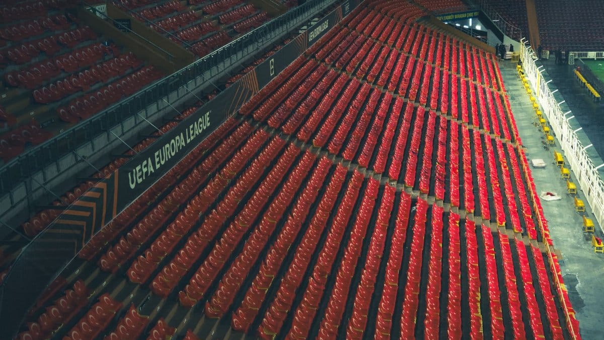 Rows of empty red seats in a UEFA Europa League stadium, captured from above.