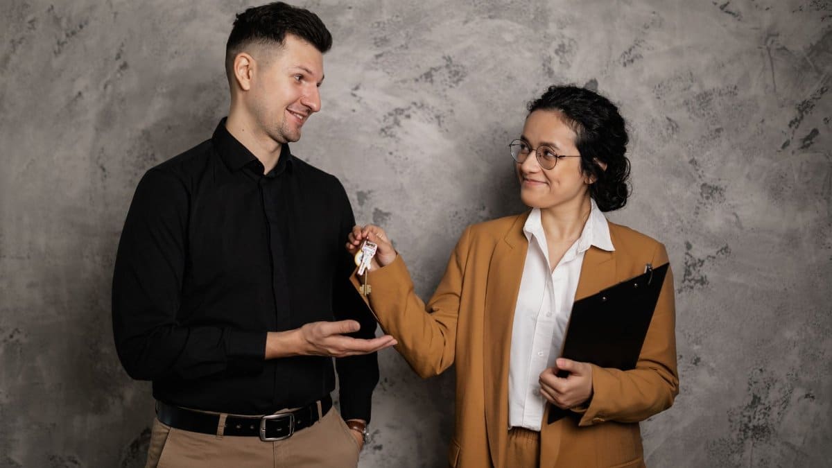 A real estate agent smiling as they hand over house keys to a new homeowner in an indoor setting.