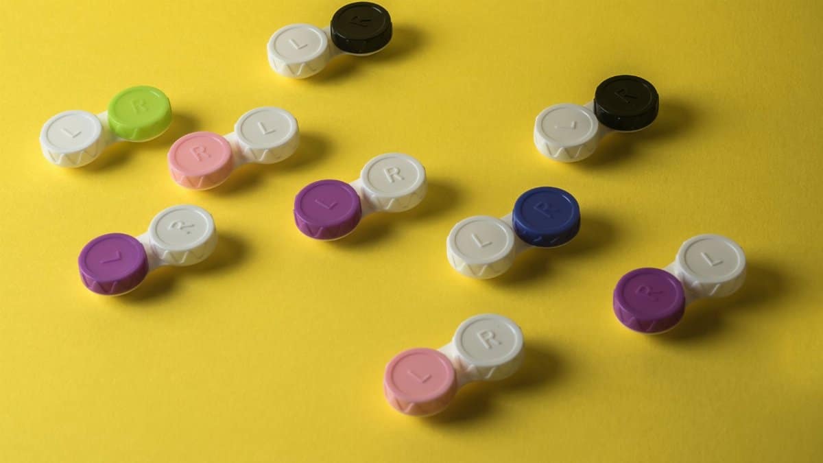 A vibrant arrangement of colorful contact lens cases on a bright yellow surface, showcasing organization.