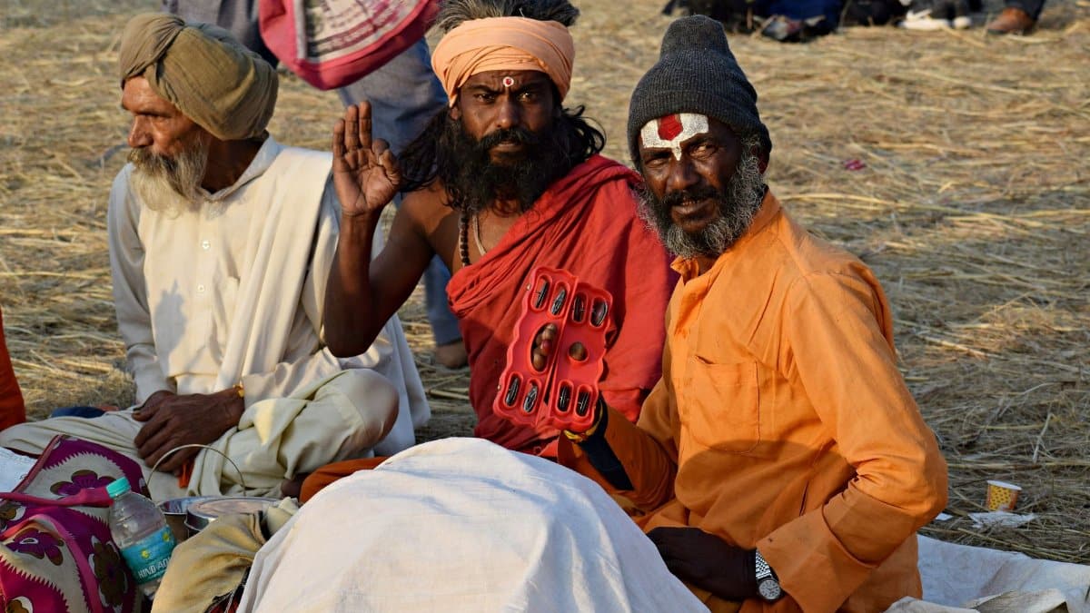 Three Indian sadhus in vibrant attire sitting on grass during the day.