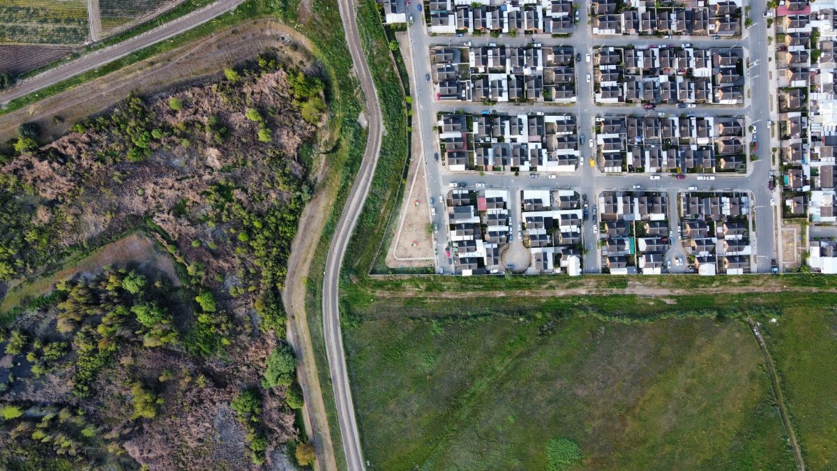 Drone view of a residential neighborhood alongside a natural landscape, showcasing urban and rural contrast.