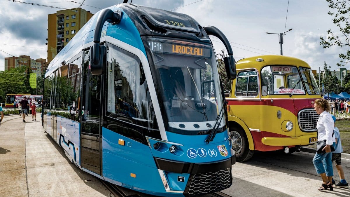 A modern tram alongside a vintage bus in Wrocław, showcasing contrast in public transportation.