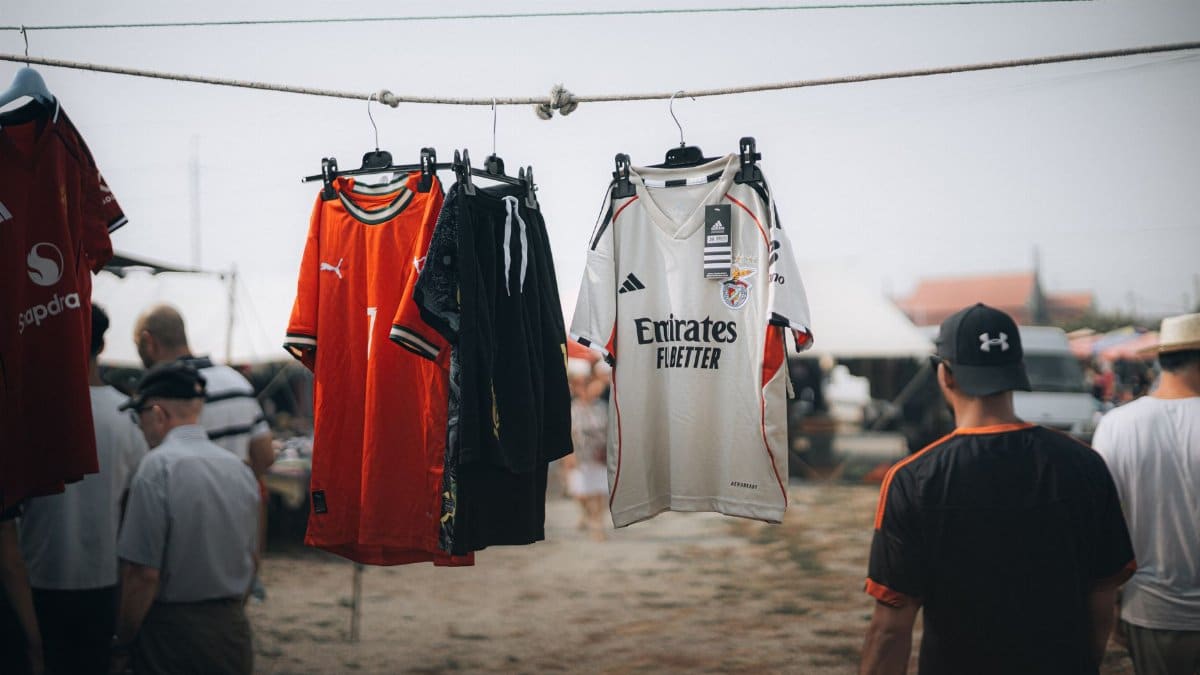 Colorful sports jerseys hanging at an outdoor market with people in the background.