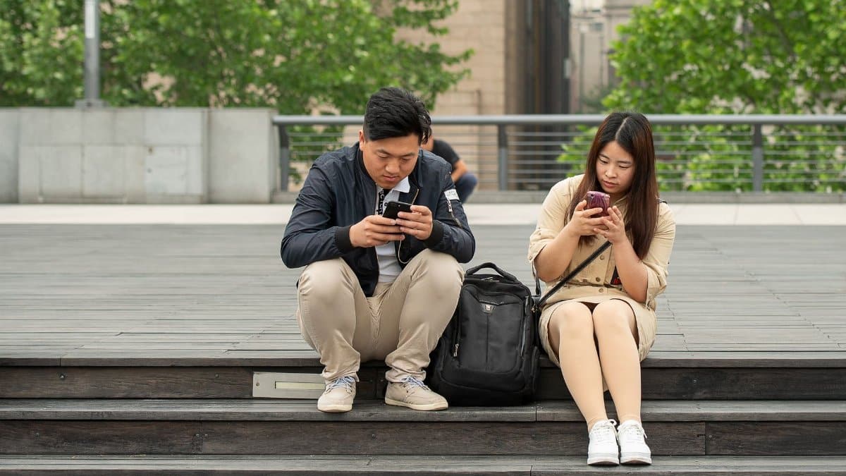Young couple absorbed in smartphones on wooden steps in urban Shanghai.