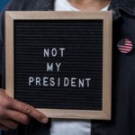 Person holding a letter board with 'Not My President' message and an American flag pin.