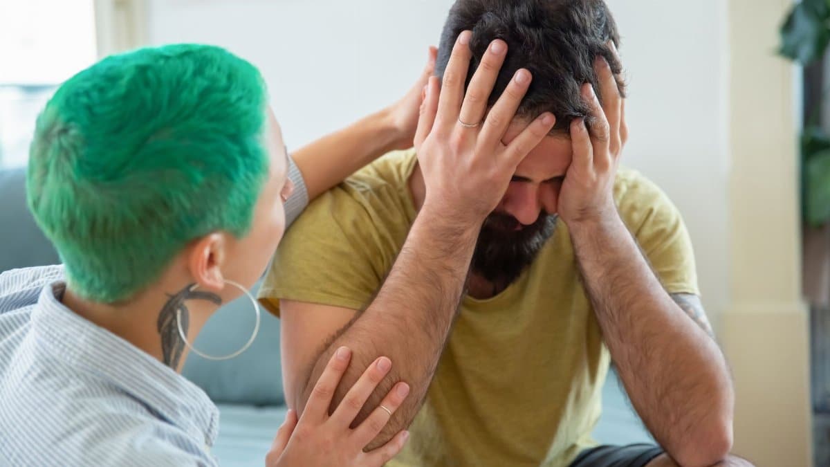 A woman with green hair offering emotional support to a distressed man indoors.