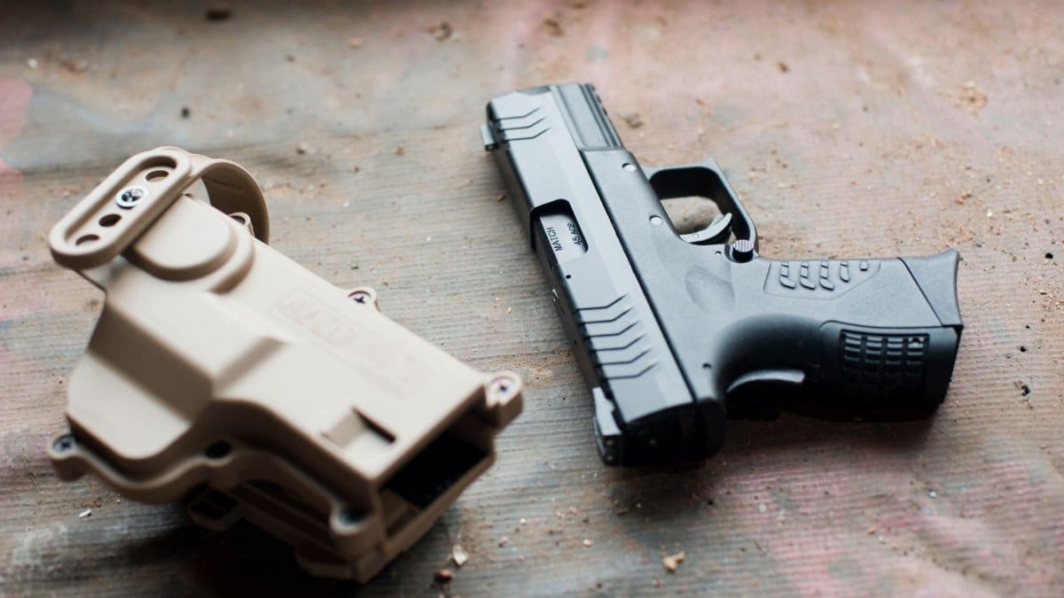 Close-up of a black handgun and beige holster on a textured surface, showcasing firearm details.
