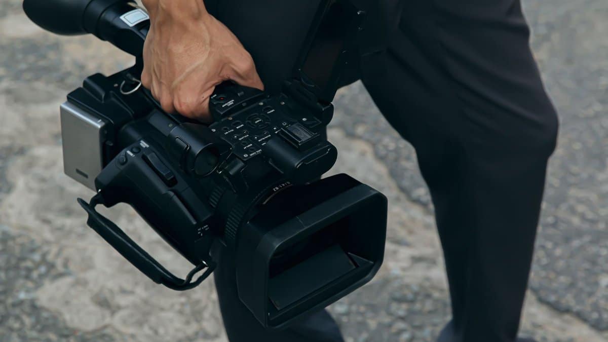 A detailed view of a person carrying a professional video camera outdoors.