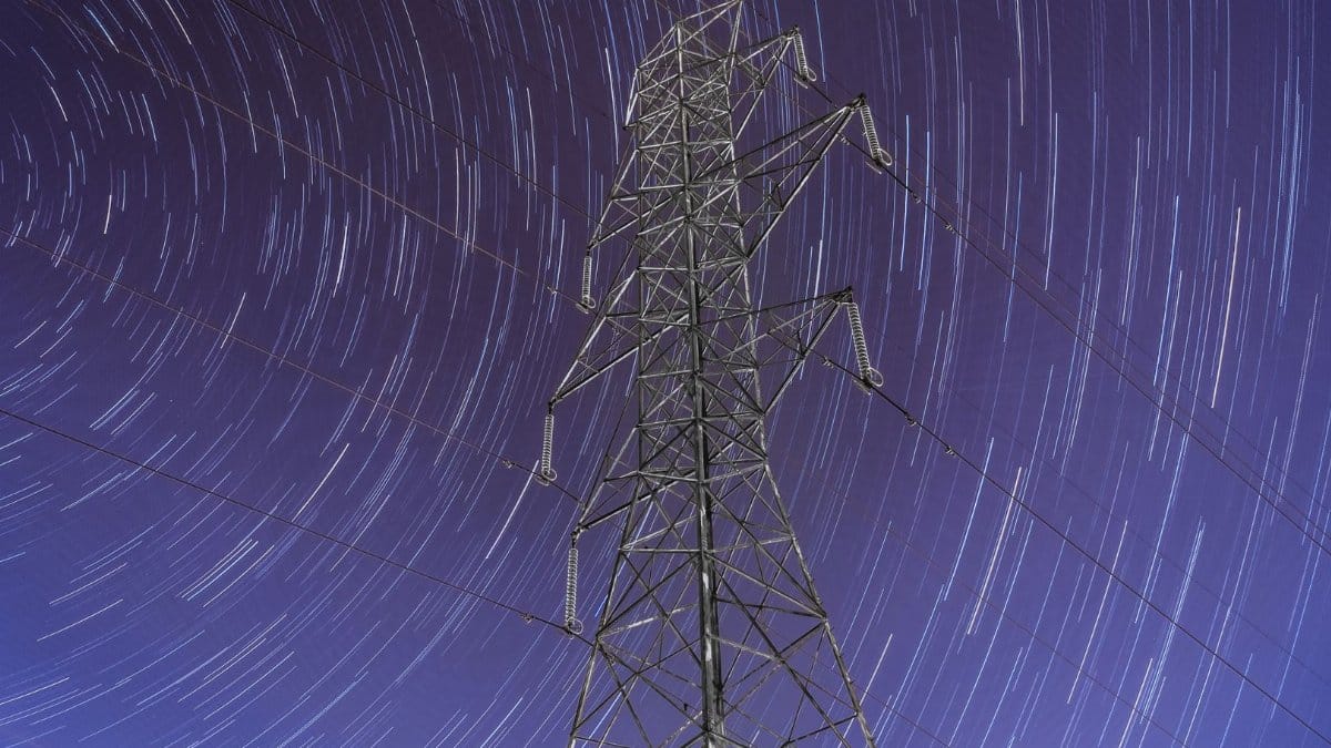Nighttime long-exposure captures star trails over a towering power pylon in Quebec City, Canada.