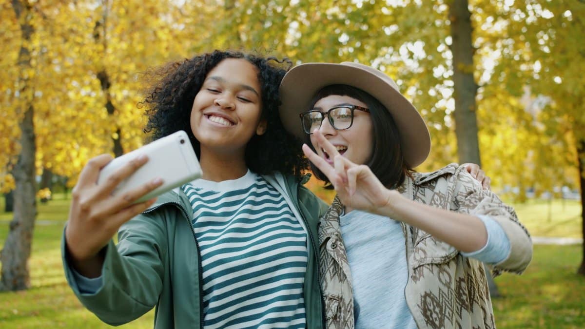 Young friends smiling and taking selfies in a vibrant autumn park.