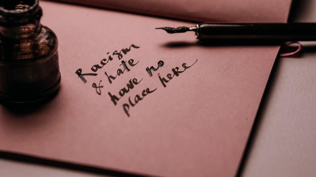 Ink pen and bottle on pink paper with motivational quote against racism and hate.