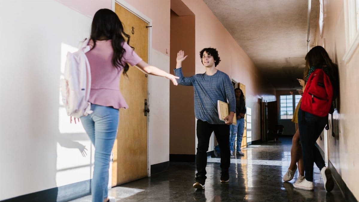 Teens greeting each other happily in a school hallway with natural light.