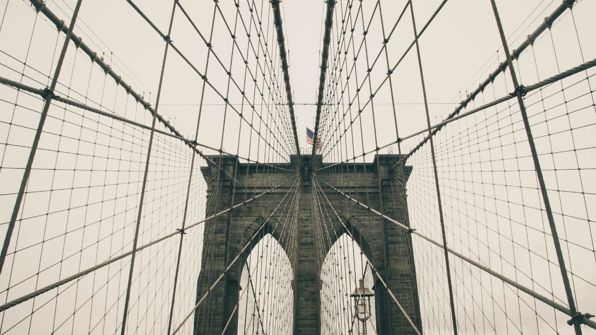 Iconic Brooklyn Bridge with American flag seen from a low angle, showcasing architectural details.