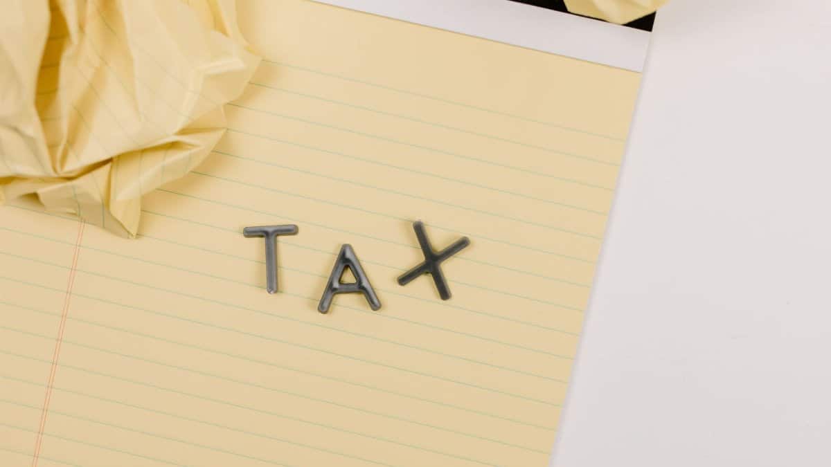 Close-up of a yellow lined paper with metal letters spelling 'tax', surrounded by crumpled paper.