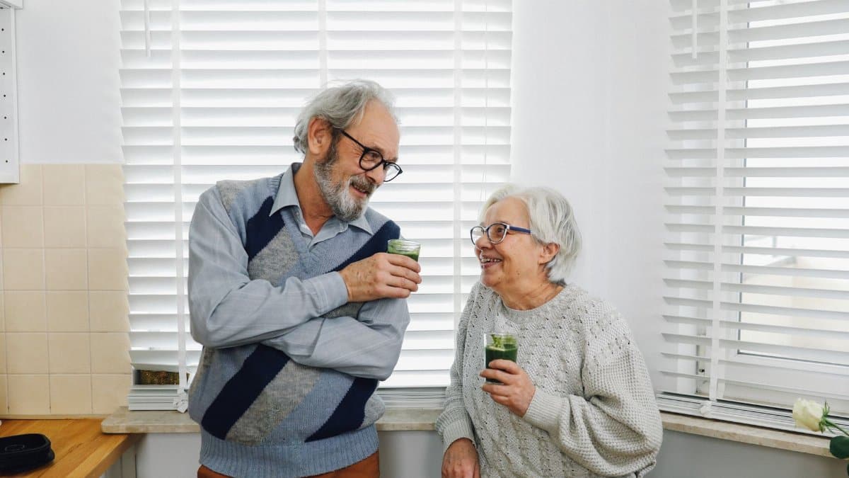 Senior couple smiling and enjoying green smoothies in a cozy kitchen setting.