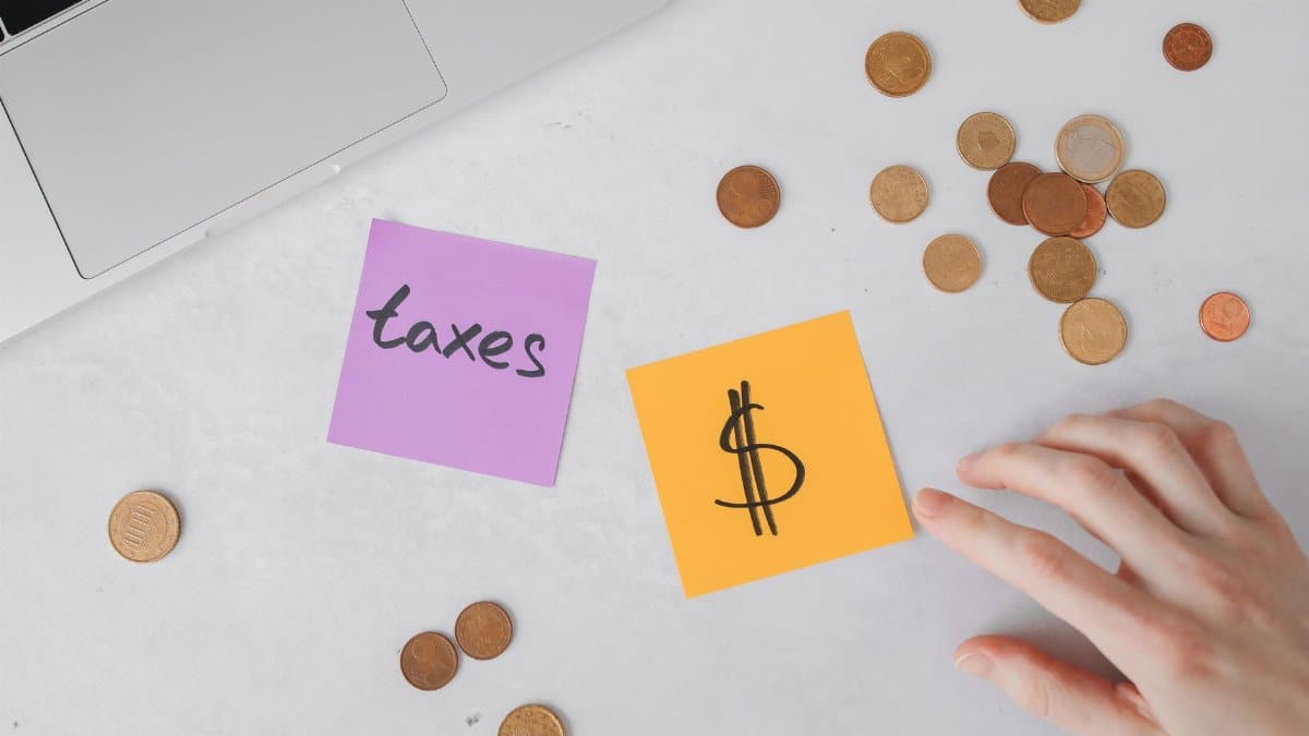Overhead view of coins, sticky notes with tax symbols, and a hand on a desk.