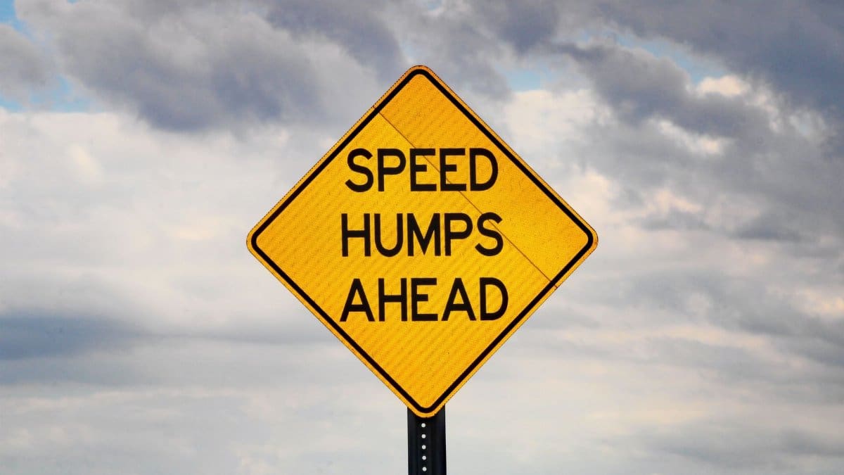 A speed hump warning sign under a cloudy sky, emphasizing safety.
