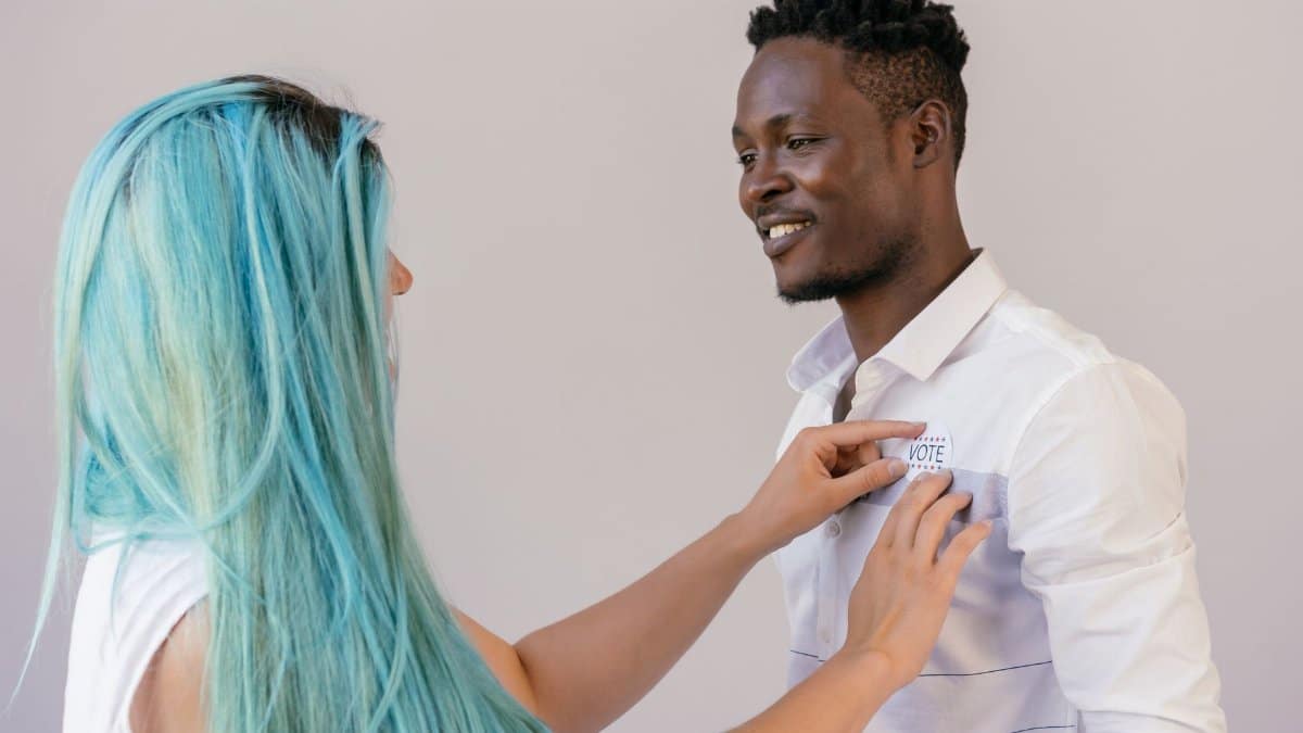 A woman pins a voting badge on a smiling man's shirt, promoting civic engagement.
