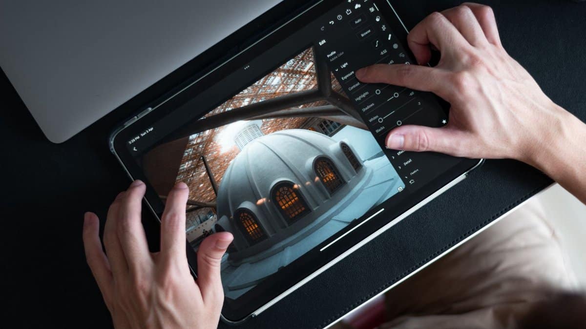 Hands editing architectural photo on tablet using Lightroom app.