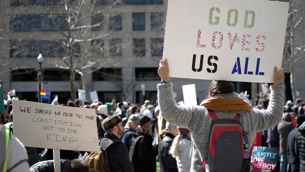 A crowd gathers for a protest in Baltimore holding signs promoting love, equality, and constitutional rights.