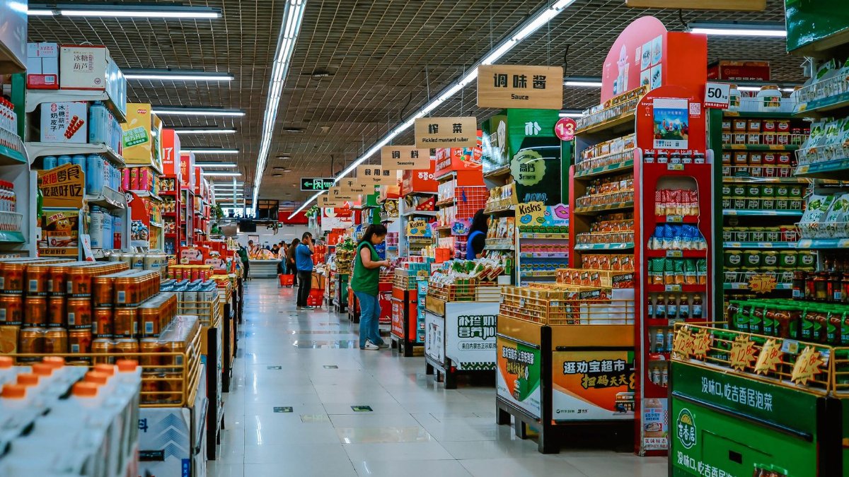 A vibrant supermarket aisle filled with diverse products and shoppers under bright lighting.