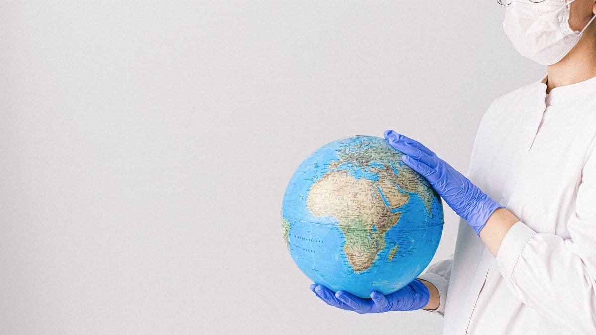 Person in mask and gloves holding a globe, symbolizing global healthcare during pandemic.
