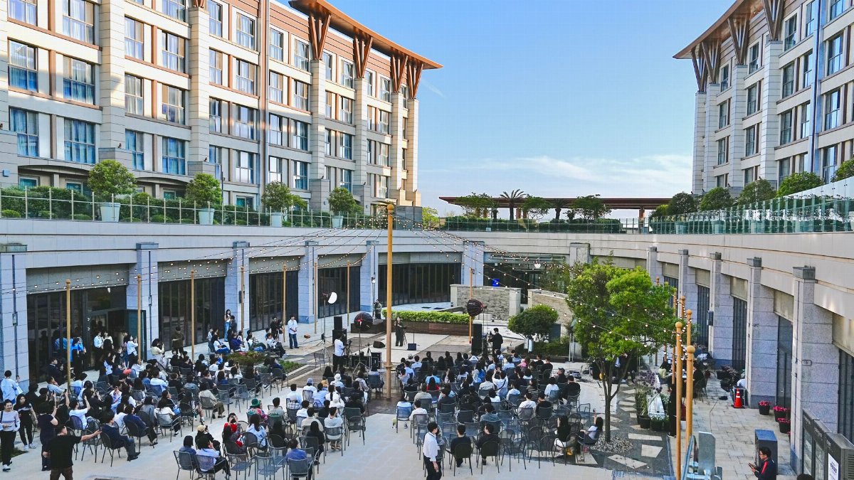 Large outdoor corporate event with attendees seated in courtyard of a modern building complex.
