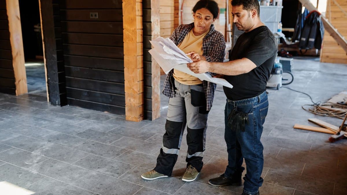 Two workers examining blueprints inside a building under construction, showcasing teamwork.