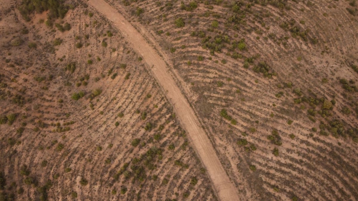 An aerial shot of a winding dirt road through a dry, rugged landscape.