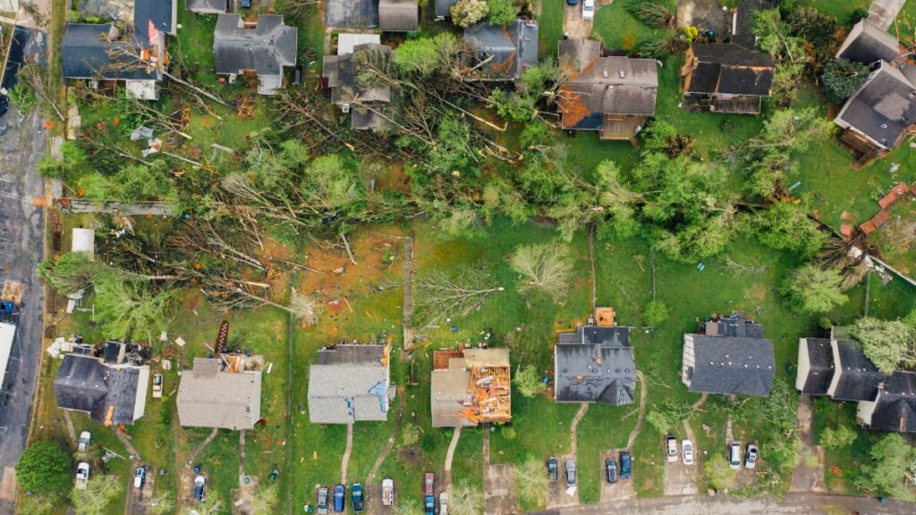 Drone dramatic view of small settlement cottages with ruined roofs and windthrown trees after massive storm