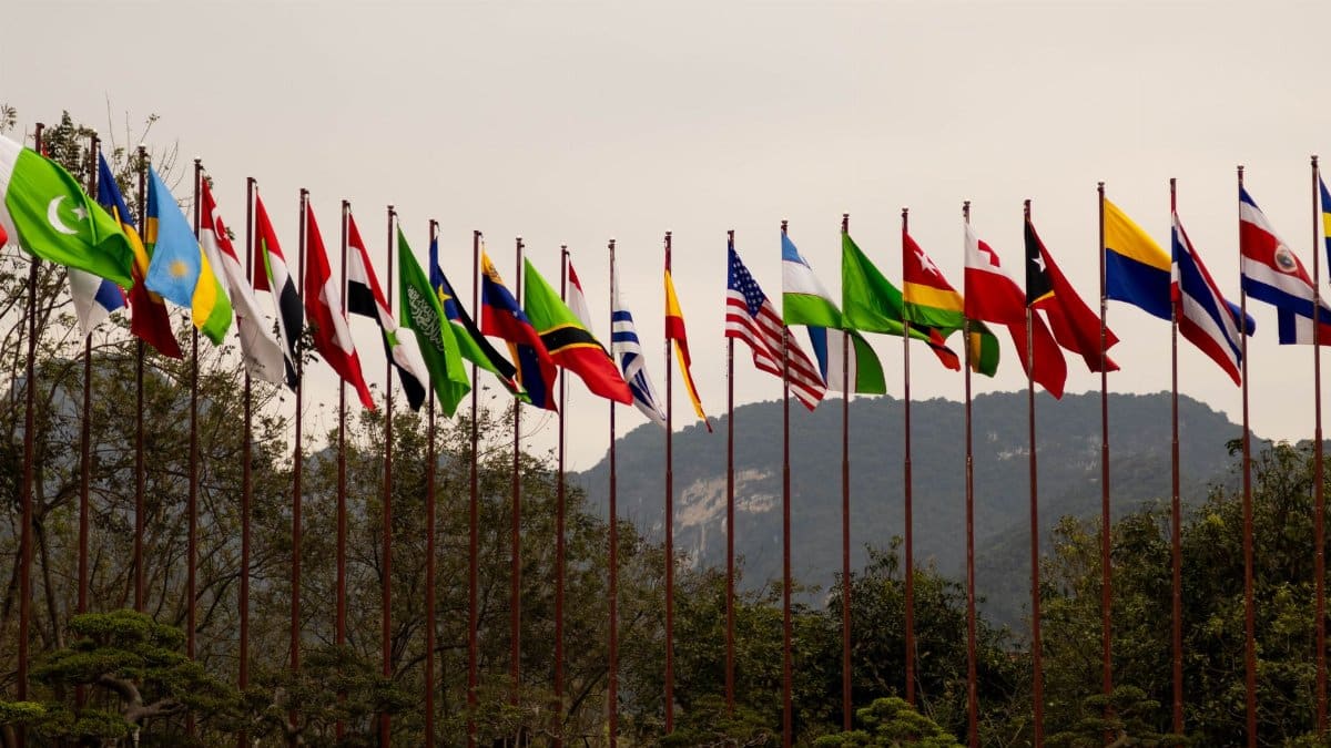 A display of various national flags on flagpoles set against a mountain backdrop, symbolizing global unity.