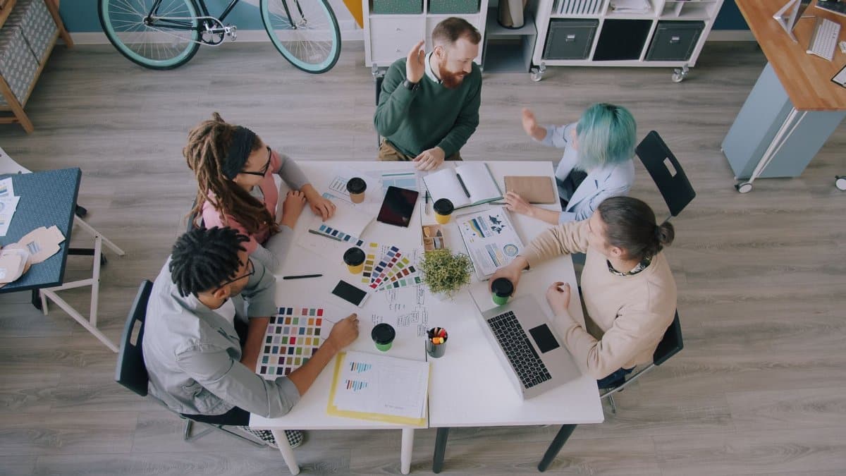 Top view of diverse creative team collaborating at a workspace with tech and charts.