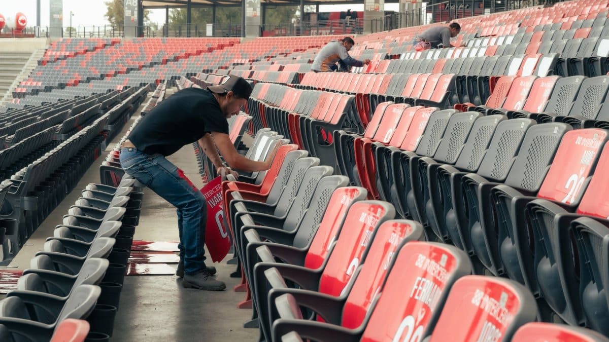 Workers preparing stadium seating for an upcoming sports event, organizing and cleaning rows of seats.