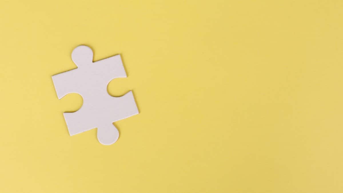 Simple white jigsaw puzzle piece placed on a bright yellow background with ample copy space.
