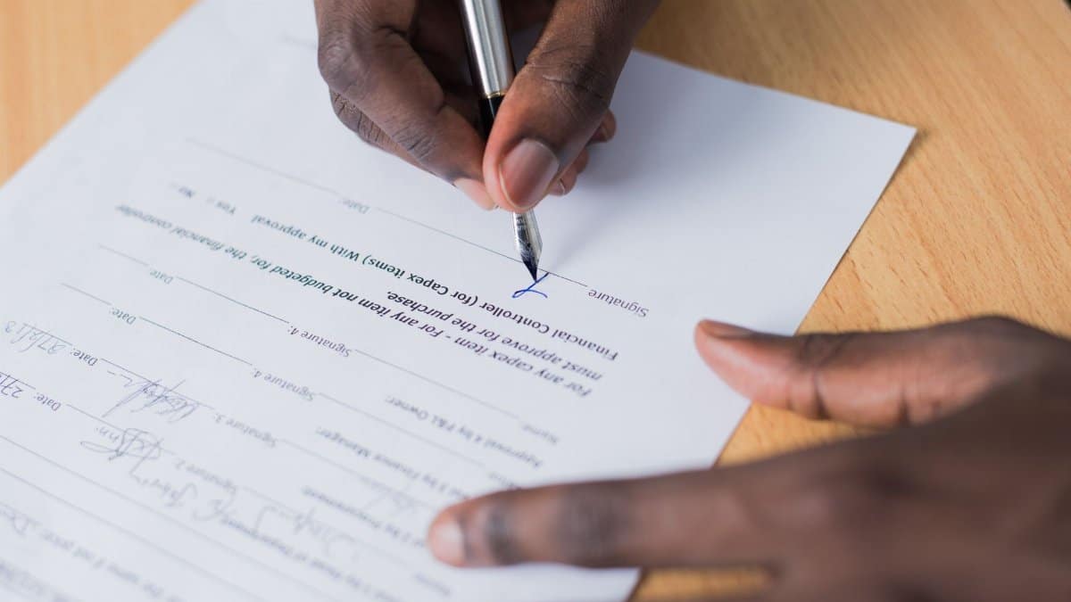 A close-up view of a person's hand signing a business contract on a desk with a pen.
