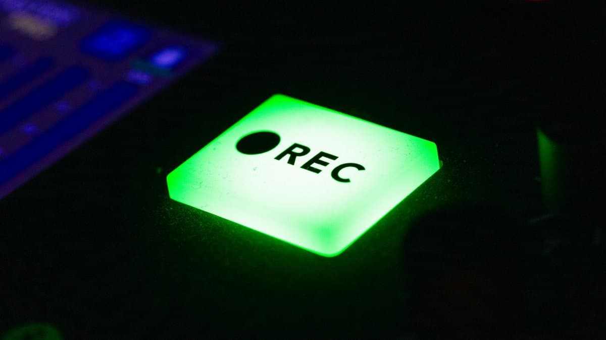 Close-up of a green illuminated recording button on electronic device in low light.