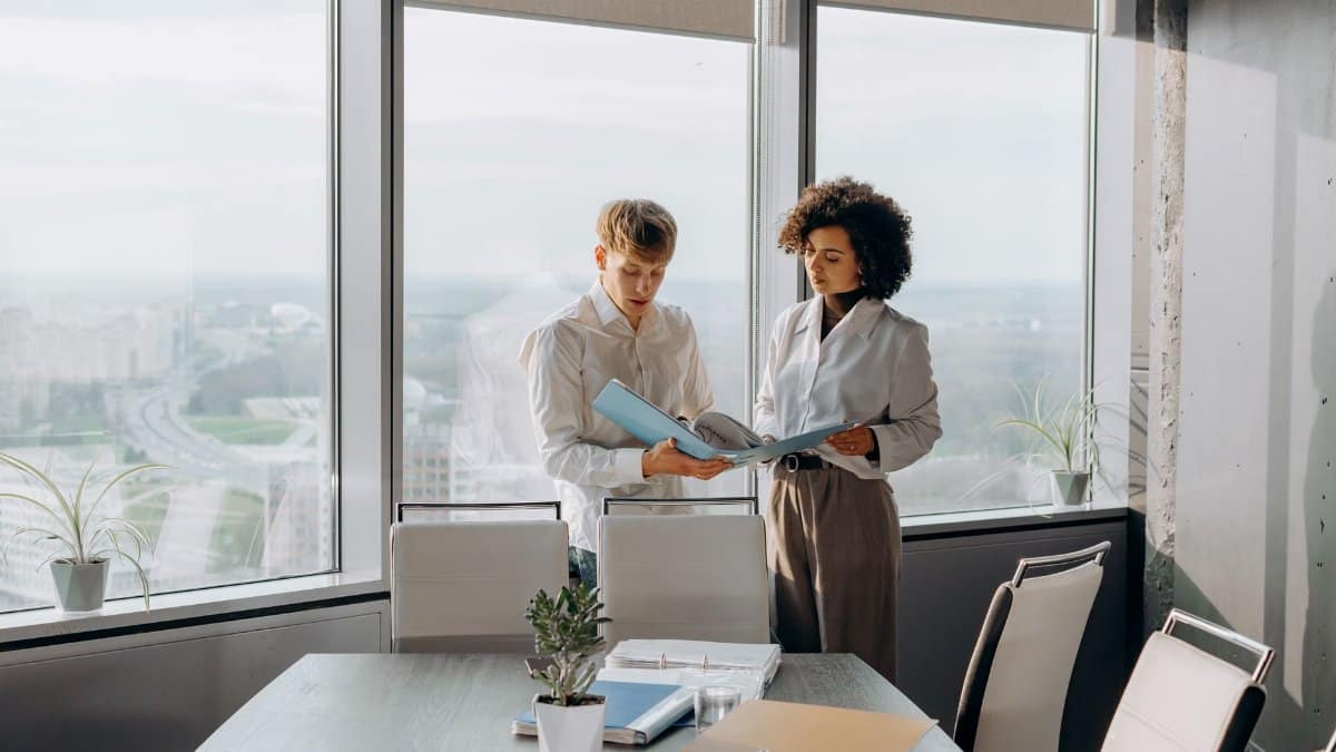 Two business professionals discussing paperwork in a bright, modern office setting.