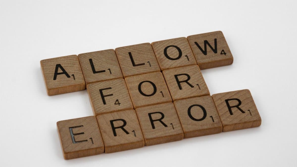 Wooden Scrabble tiles spelling 'Allow for Error' on a white surface.