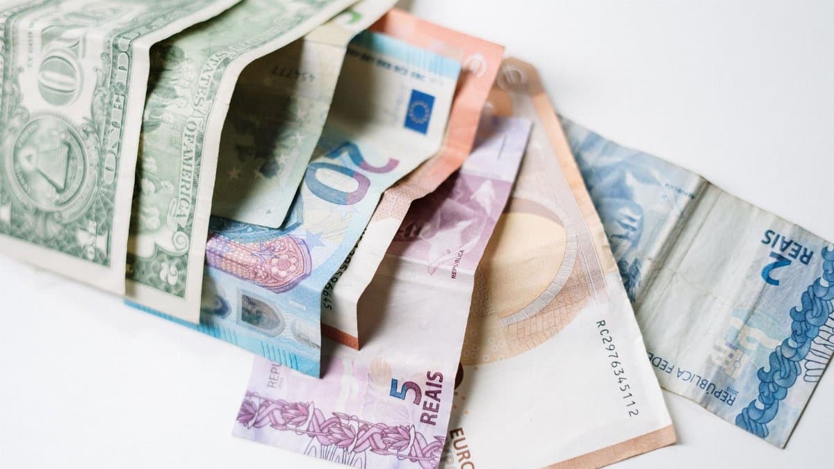 A collection of different international currency notes, including US Dollar, Euro, and Brazilian Real, on a white background.