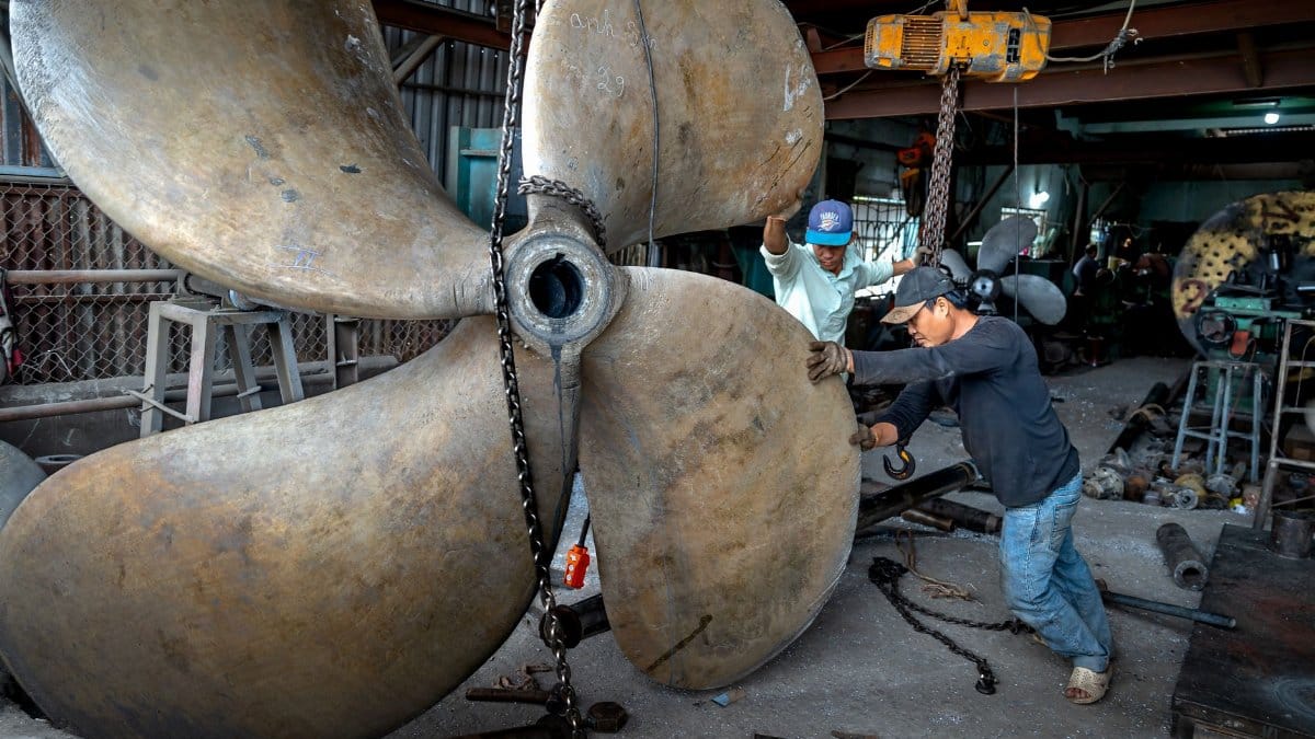 Two men working together to handle a massive industrial propeller in a workshop setting.