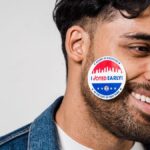 Smiling young man with 'I Voted Early' sticker on cheek, demonstrating civic participation.