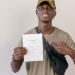 Young adult smiling and pointing at electoral ballot paper, emphasizing the importance of voting.