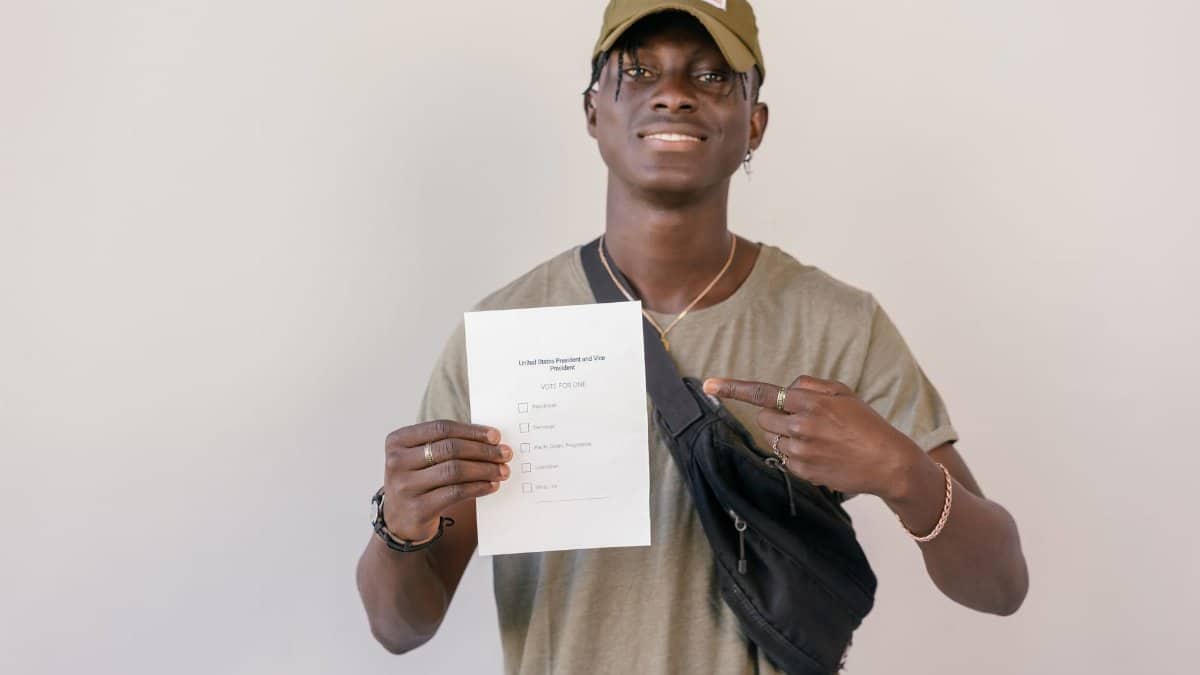 Young adult smiling and pointing at electoral ballot paper, emphasizing the importance of voting.